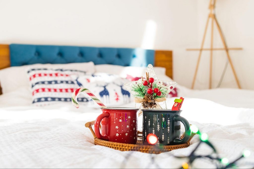Holiday mugs with hot drinks and festive treats arranged on a guest room bed.
© nikolast1