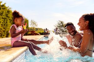 Family playing and splashing in a community pool on a sunny day. ©Monkey Business Images