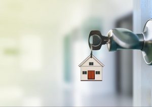 A key in a door with a small house keychain, symbolizing new homeownership. ©Naypong Studio
