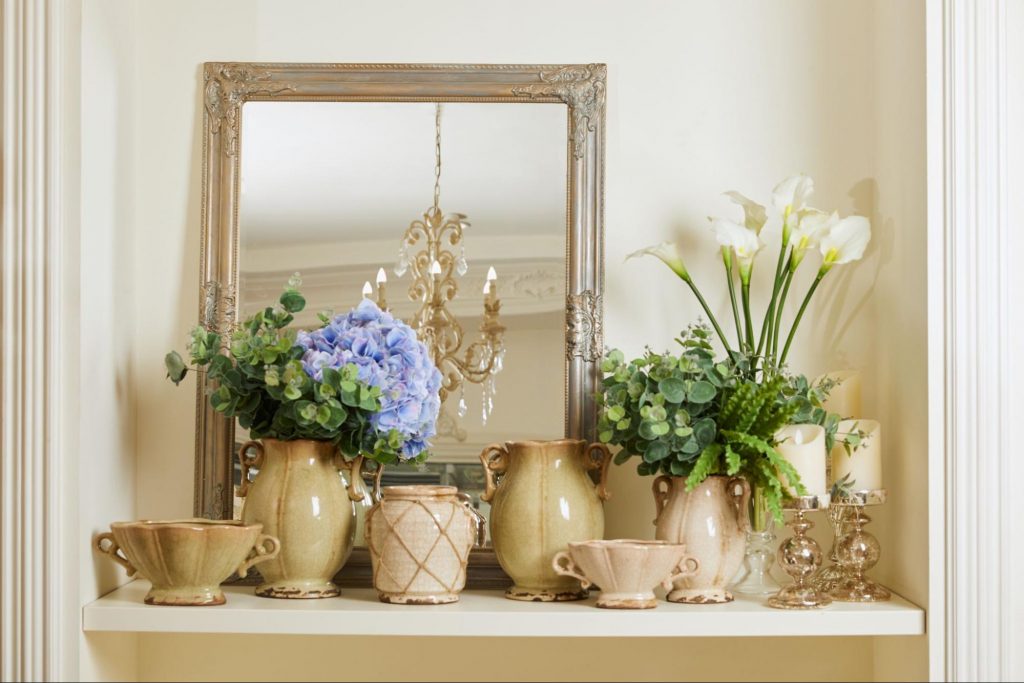 Antique mirror with thrifted vases, candlesticks, and decorative flowers in front.
© LightFieldStudios