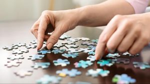 Hands assembling a complex jigsaw puzzle on a table during a phone free afternoon. ©Prostock-studio