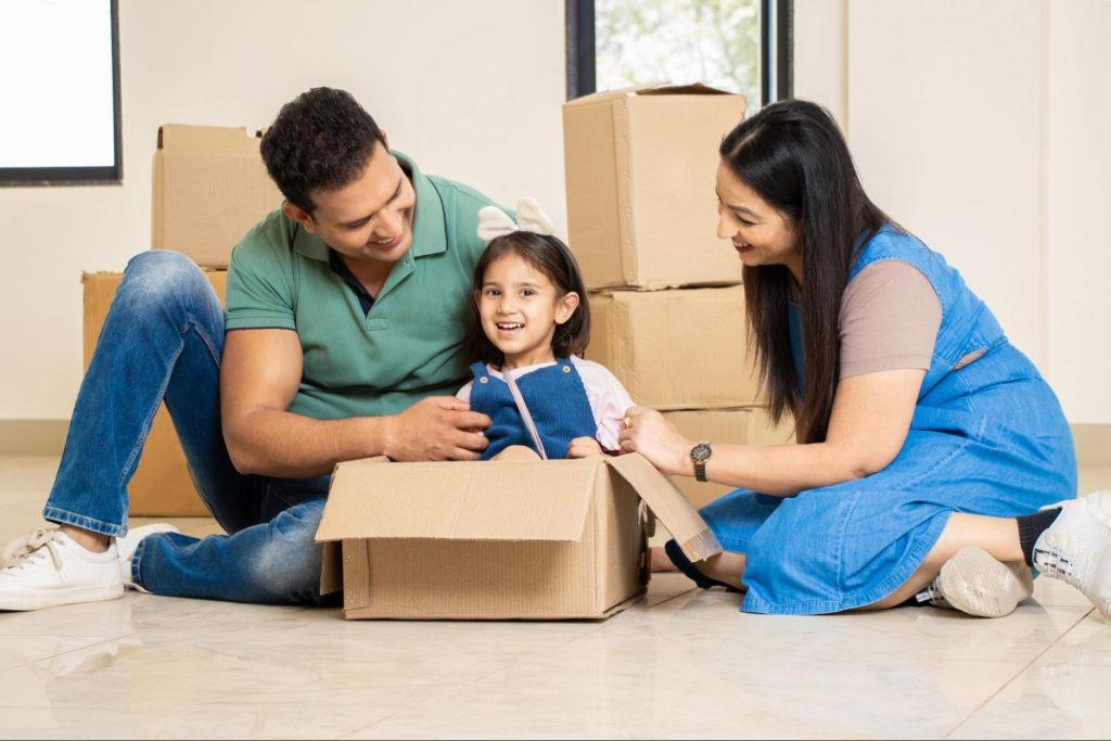 A happy family sitting among cardboard moving boxes, representing the excitement of moving into a new construction home in Forsyth County, GA. ©stockpexel