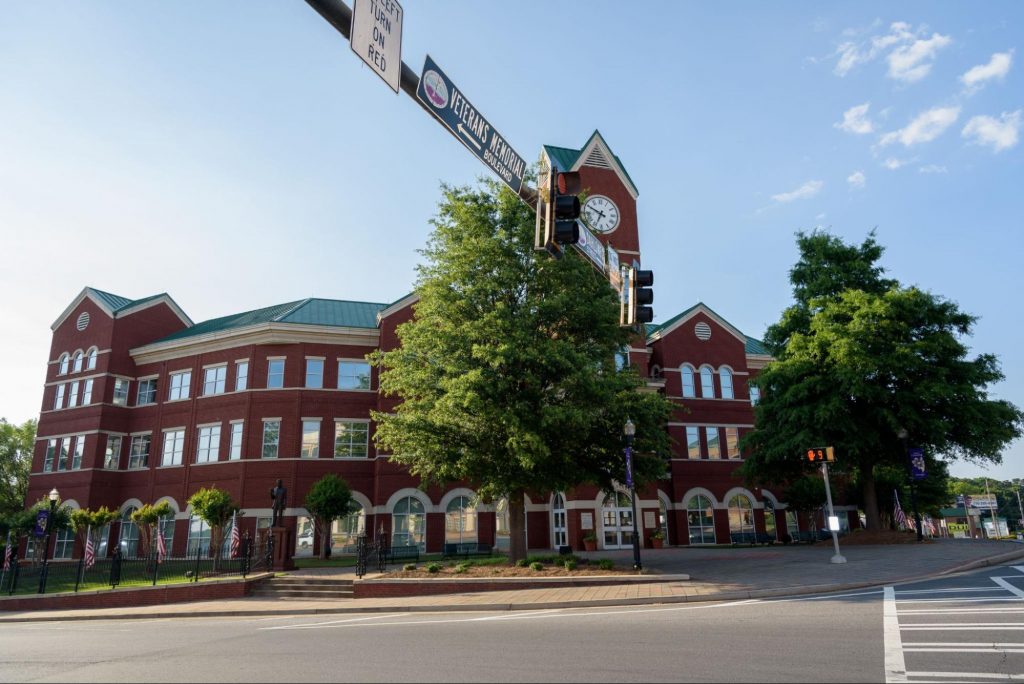 street view of downtown Cumming, GA featuring a brick building and clock tower under a partly cloudy blue sky, showcasing the local charm of Forsyth County. ©RodClementPhotography